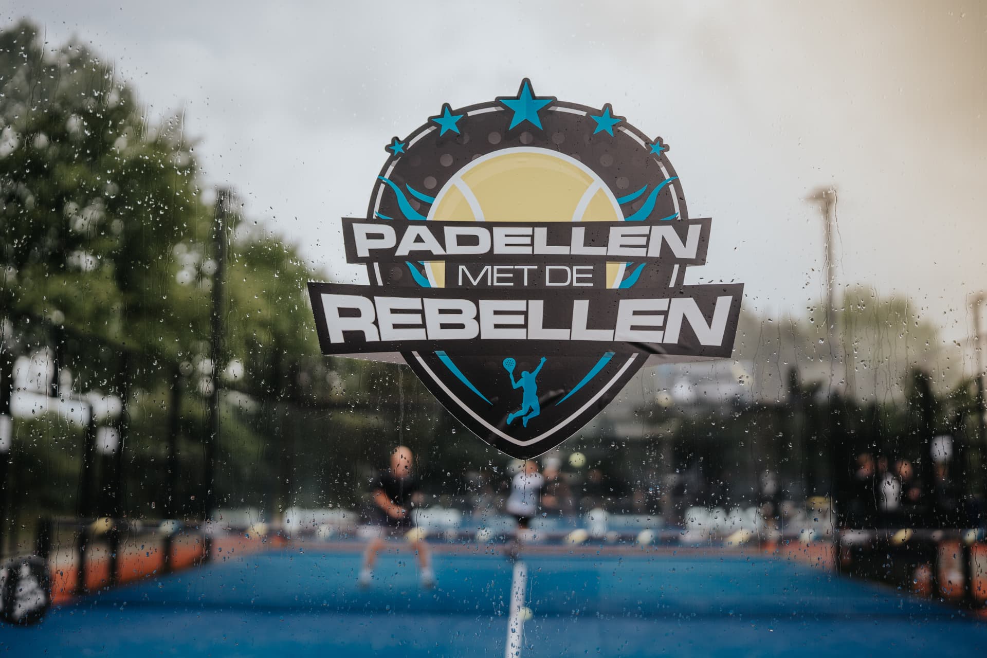 Padellen met de Rebellen event identity on a rainy padel court window